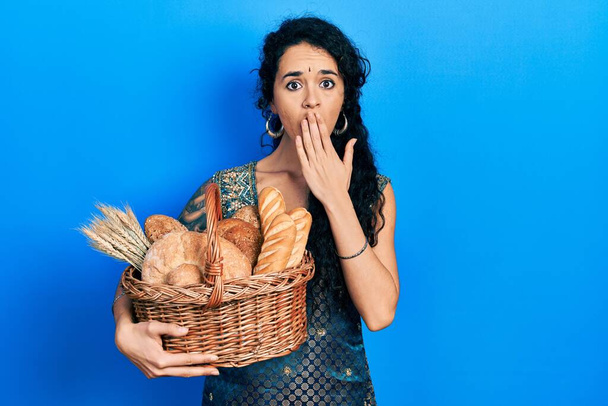 junge Frau in Bindi und traditioneller Kurta-Tracht mit Weidenkorb und Brotdeckel in der Hand, schockiert und verängstigt über Fehler. Überraschte Miene  - Foto, Bild