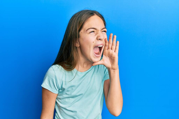 Beautiful brunette little girl wearing casual white t shirt shouting and screaming loud to side with hand on mouth. communication concept.  - Photo, Image