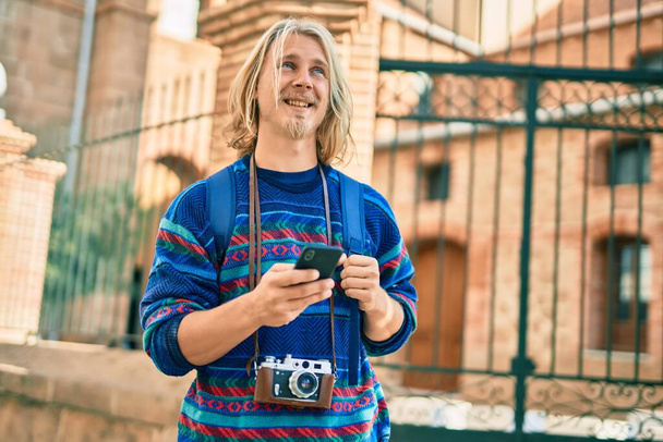 Fiatal skandináv turista férfi mosolyog boldog segítségével smartphone a városban. - Fotó, kép