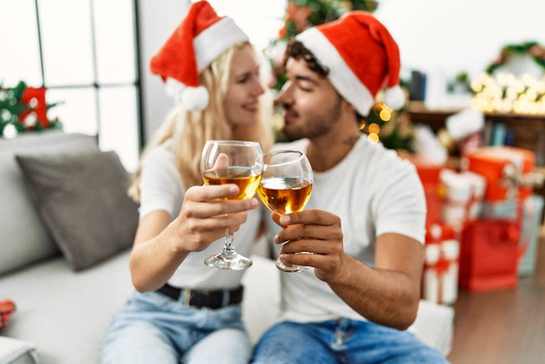 Junges Paar lächelt glücklich mit Weihnachtsmütze und stößt zu Hause mit Champagner an - Foto, Bild