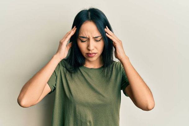 Jeune fille hispanique portant t-shirt décontracté avec la main sur la tête pour la douleur à la tête parce que le stress. migraine souffrant.  - Photo, image