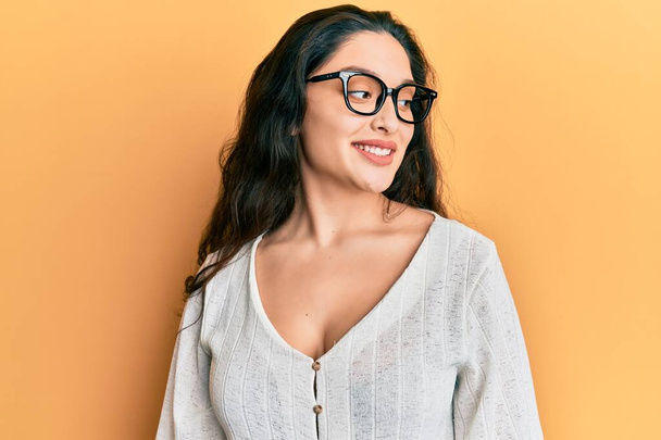 Bella donna mediorientale indossa abiti casual e occhiali cercando di lato, posa profilo relax con viso naturale e sorriso fiducioso.  - Foto, immagini