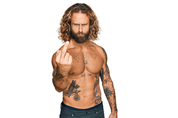 Handsome man with beard and long hair standing shirtless showing tattoos showing middle finger, impolite and rude fuck off expression  - Fotoğraf, Görsel