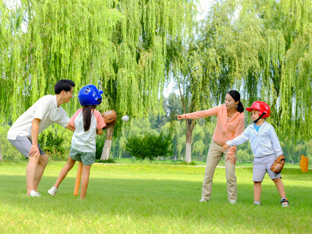 Happy family of four playing baseball in the park - Foto, afbeelding