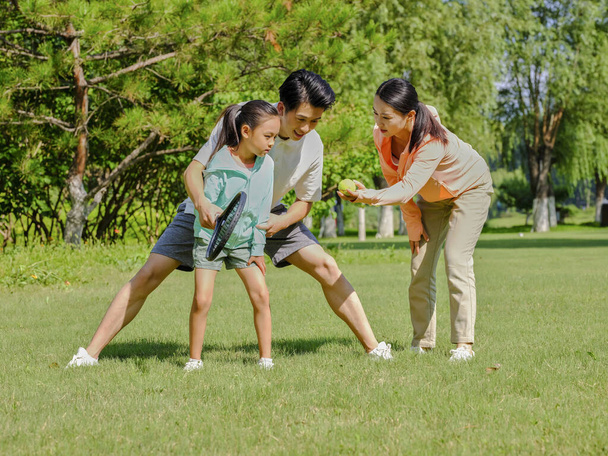Happy family of three playing tennis in the park - Photo, image