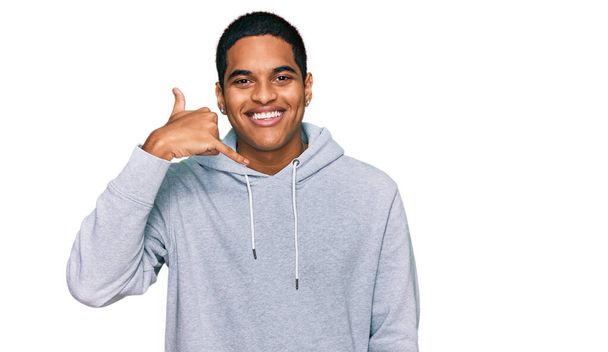 Young handsome hispanic man wearing casual sweatshirt smiling doing phone gesture with hand and fingers like talking on the telephone. communicating concepts.  - Foto, Bild