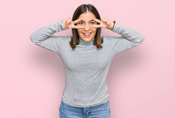 Young beautiful woman wearing casual turtleneck sweater doing peace symbol with fingers over face, smiling cheerful showing victory  - Foto, afbeelding