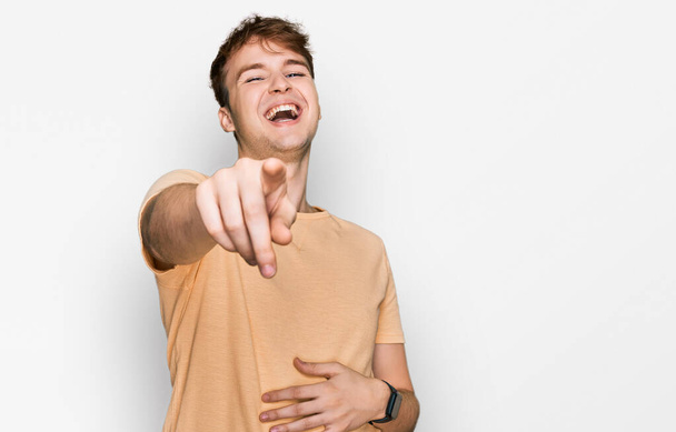 Young caucasian man wearing casual clothes laughing at you, pointing finger to the camera with hand over body, shame expression  - Photo, Image