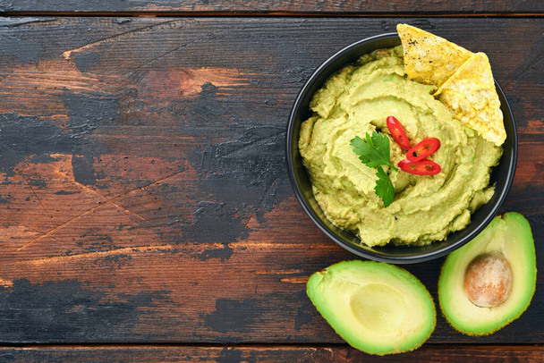 Guacamole. Traditional latinamerican Mexican dip sauce in a black bowl with avocado and ingredients and corn nachos. Avocado spread. Top view. Copyspace - Photo, Image