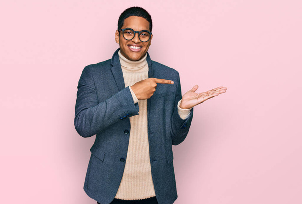 Nuori komea latino mies yllään liike takki ja lasit hämmästynyt ja hymyillen kameralle samalla esittää käsi ja sormella.  - Valokuva, kuva