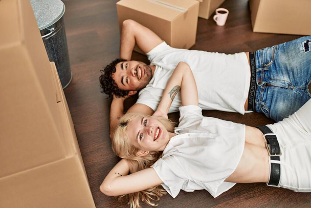 Young beautiful couple smiling happy relaxing with hands on head lying on the floor at new home. - Photo, Image