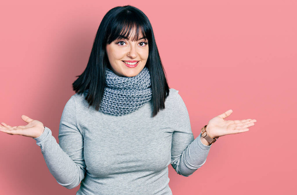Młoda Latynoska plus size kobieta w zimowym szaliku uśmiechnięta z otwartymi dłońmi, prezentująca i reklamująca porównanie i równowagę  - Zdjęcie, obraz