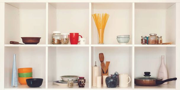 Kitchen utensils and tableware on white shelves. Well organized kitchen concept. Modern interior. Open cupboard with clean dishes. Open shelves in the kitchen. - Photo, Image