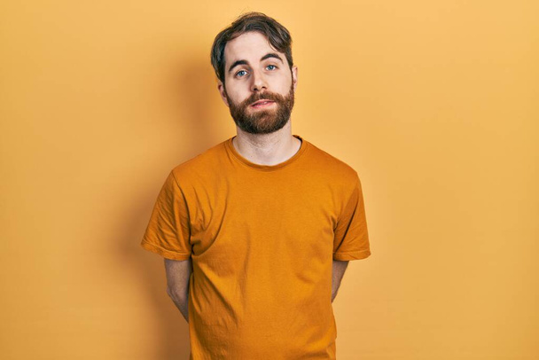 Uomo caucasico con barba che indossa casual t shirt gialla rilassata con espressione seria sul viso. semplice e naturale guardando la fotocamera.  - Foto, immagini