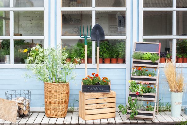 Exterior varanda de madeira de casa com plantas verdes e flores em caixa. Fachada casa com ferramentas de jardim, cesta de vime e vasos de flores. Casa de varanda aconchegante decoração de verão. Conceito de jardinagem. Pátio de rua - Foto, Imagem