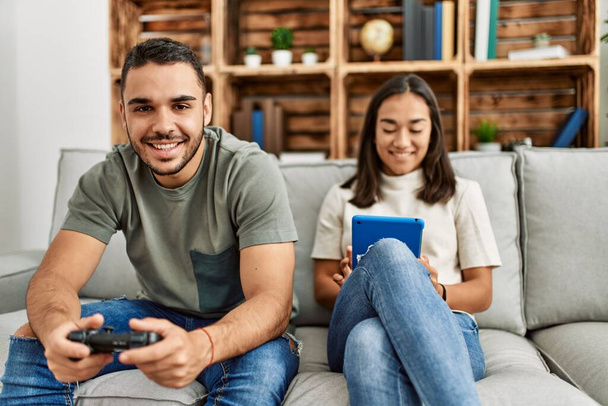 Νεαρό λατινικό ζευγάρι παίζει βιντεοπαιχνίδι και χρησιμοποιεί touchpad στο σπίτι. - Φωτογραφία, εικόνα