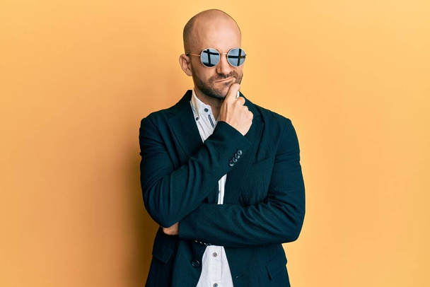 Jonge Latijns-Amerikaanse man draagt mode zonnebril en business jas denken geconcentreerd over twijfel met de vinger op de kin en kijken omhoog afvragen  - Foto, afbeelding