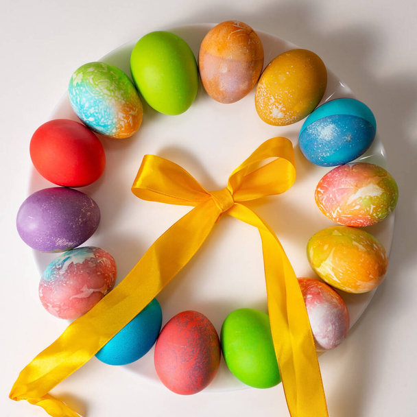 Кольорові яйця на Великдень на білому тлі, розкидані по колу, оточені кольоровими стрічками
  - Фото, зображення
