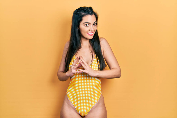 Young hispanic girl wearing swimsuit hands together and fingers crossed smiling relaxed and cheerful. success and optimistic  - Fotografie, Obrázek