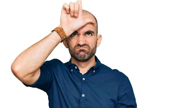 Young hispanic man wearing casual clothes making fun of people with fingers on forehead doing loser gesture mocking and insulting.  - Photo, Image