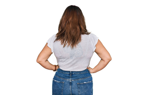 Молода жінка плюс розмір в повсякденній білій сорочці, стоячи позаду, дивлячись з руками на тіло
  - Фото, зображення