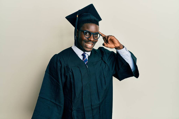 Handsome black man wearing graduation cap and ceremony robe smiling pointing to head with one finger, great idea or thought, good memory  - Foto, immagini