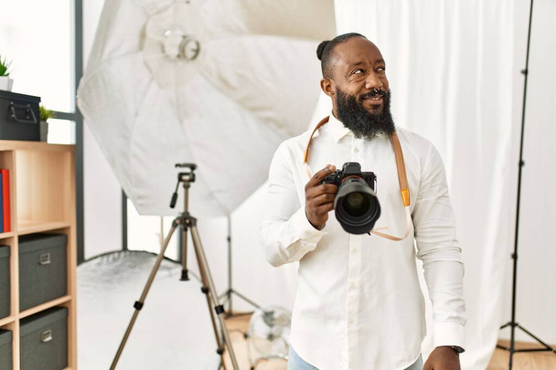 Afrikai amerikai fotós férfi dolgozik fotózás stúdió mosolyog oldalra néz, és bámul félre gondolkodás.  - Fotó, kép
