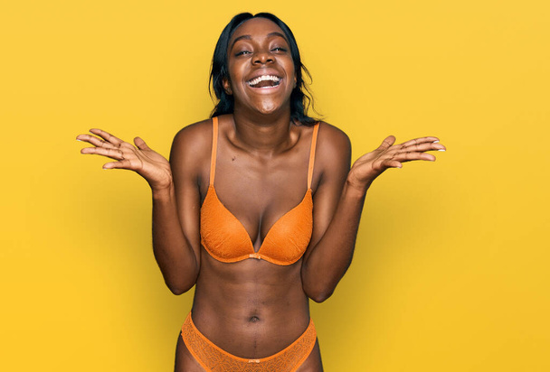 Jovem afro-americana vestindo lingerie celebrando louco e espantado com o sucesso com os braços levantados e os olhos abertos gritando animado. conceito vencedor  - Foto, Imagem