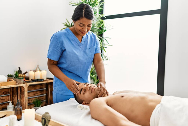 Молодая женщина-терапевт латинского массажа проводит расслабляющее лечение на голове мужчины в салоне красоты. - Фото, изображение
