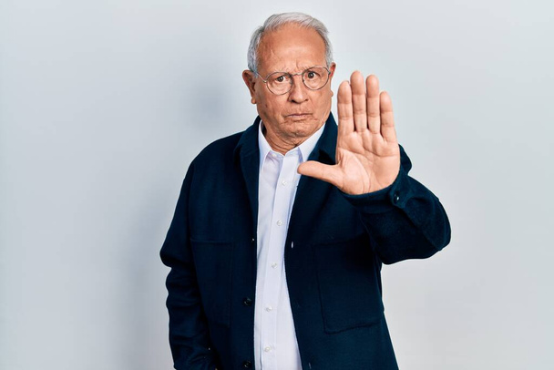 Senior man with grey hair wearing casual style and glasses doing stop sing with palm of the hand. warning expression with negative and serious gesture on the face.  - Photo, image