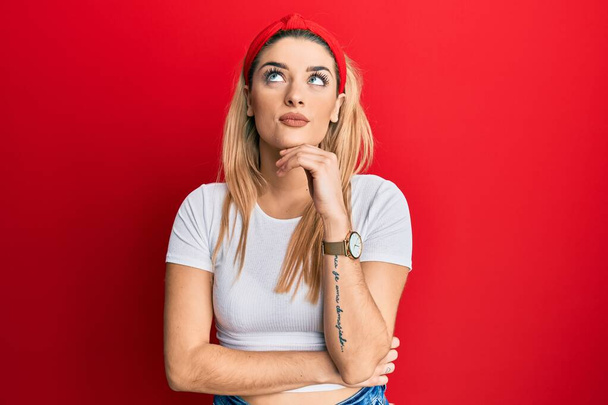 Young caucasian woman wearing casual white t shirt with hand on chin thinking about question, pensive expression. smiling and thoughtful face. doubt concept.  - Photo, Image