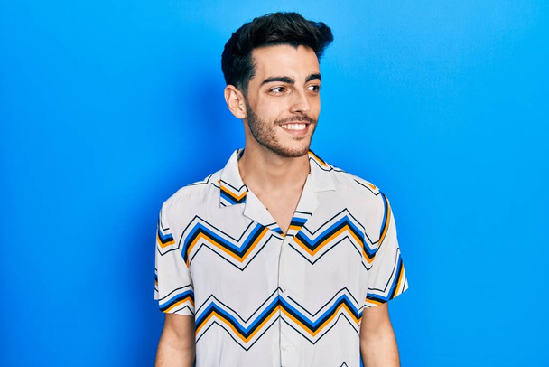 Jonge Latijns-Amerikaanse man met casual kleren die van achteren kijken met een glimlach op het gezicht, natuurlijke expressie. lachen vol vertrouwen.  - Foto, afbeelding