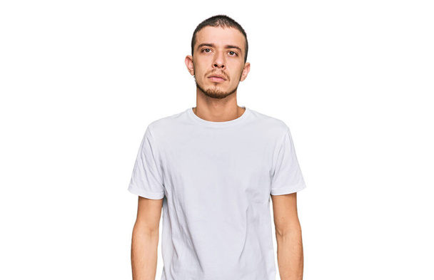 Hispanic young man wearing casual white t shirt relaxed with serious expression on face. simple and natural looking at the camera.  - Fotó, kép