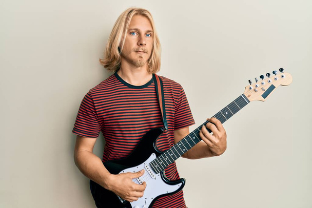 Caucasian young man with long hair playing electric guitar relaxed with serious expression on face. simple and natural looking at the camera.  - Photo, Image