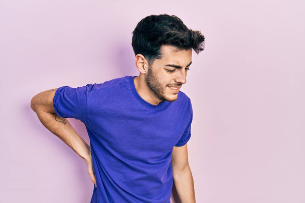 Junger hispanischer Mann in lässigem T-Shirt mit Rückenschmerzen, Berührung des Rückens mit der Hand, Muskelschmerzen  - Foto, Bild
