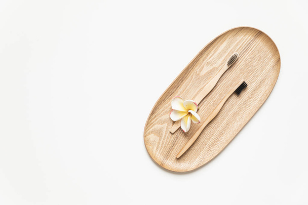 Bamboo toothbrush on a table with copy space on a white background. Styled composition of flat lay with tropical flowers. - Fotó, kép