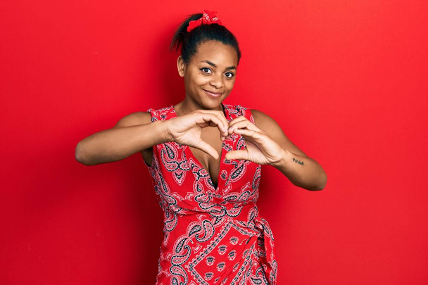 若いアフリカ系アメリカ人の少女は、愛の心のシンボルと手で形を示す笑みを浮かべてカジュアルな服を着て。ロマンチックなコンセプト.  - 写真・画像