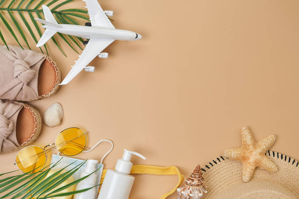 sun protection cream, sunglasses, seashell and starfish, summer shoes and surgical mask and airplane on beige sand background. Summer flat lay. copy space. Trendy Sun protection accessory. - Photo, Image