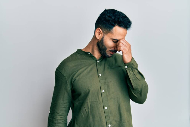 Young hispanic man wearing casual clothes tired rubbing nose and eyes feeling fatigue and headache. stress and frustration concept.  - Photo, image