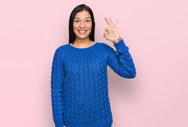 Молодая латиноамериканка в повседневной одежде, улыбающаяся позитивно, делает знак "хорошо" с рукой и пальцами. успешное выражение.  - Фото, изображение