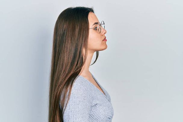 Mladá brunetka teenager nosit ležérní svetr a brýle hledá na stranu, relaxační profil pózovat s přirozenou tváří s sebevědomým úsměvem.  - Fotografie, Obrázek
