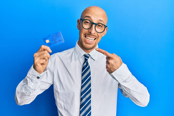 Bald man with beard holding credit card smiling happy pointing with hand and finger  - 写真・画像