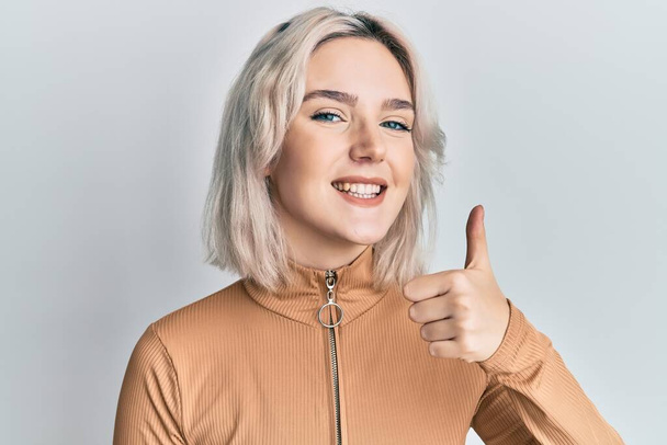 Young blonde girl wearing casual clothes doing happy thumbs up gesture with hand. approving expression looking at the camera showing success.  - Photo, Image