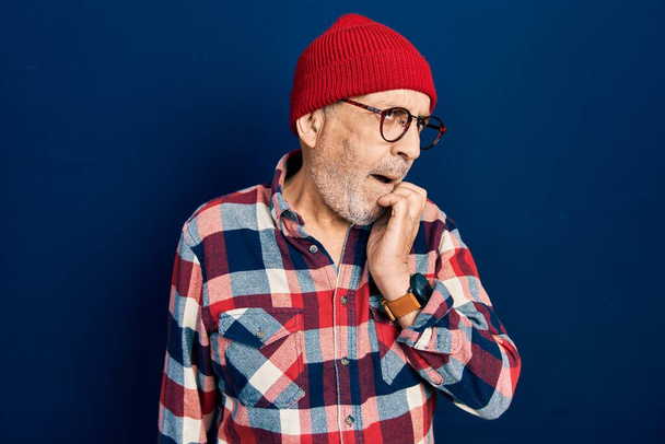 Handsome mature man wearing hipster look with wool cap looking stressed and nervous with hands on mouth biting nails. anxiety problem.  - Photo, Image