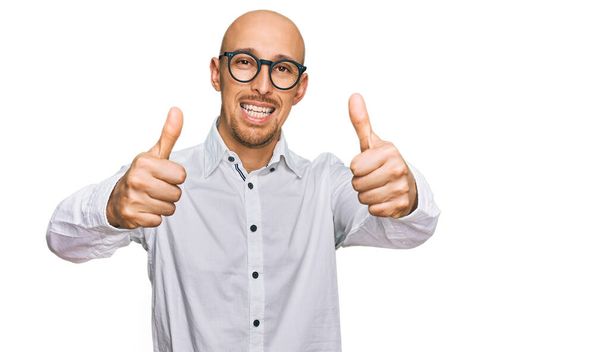 Glatzköpfiger Mann mit Bart, Businesshemd und Brille, der zustimmend positive Gesten mit der Hand macht, Daumen hoch lächelnd und glücklich über den Erfolg. Siegergeste.  - Foto, Bild