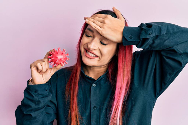 Jovem mulher caucasiana segurando vírus brinquedo estressado e frustrado com a mão na cabeça, rosto surpreso e irritado  - Foto, Imagem