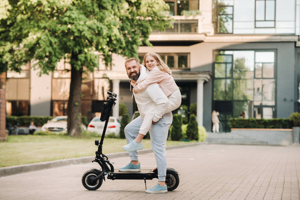 Een familie in witte kleren staat in de stad op elektrische scooters.Vader en dochter op een elektrische scooter. - Foto, afbeelding