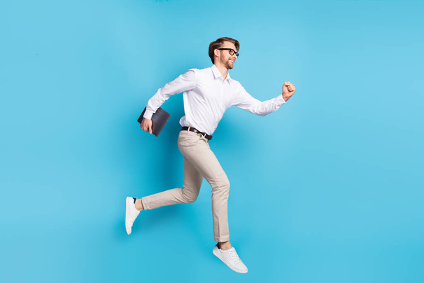 Full length body size view of attractive cheerful man jumping running carrying laptop isolated over bright blue color background - Фото, зображення