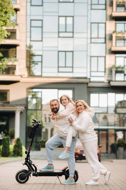 A family in white clothes stands in the city on electric scooters. - Foto, Imagem