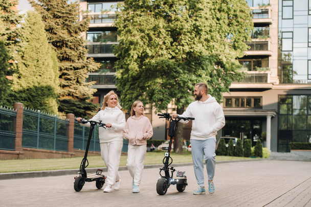 A family in white clothes rides electric scooters in the city.Outdoor activities. - Фото, изображение